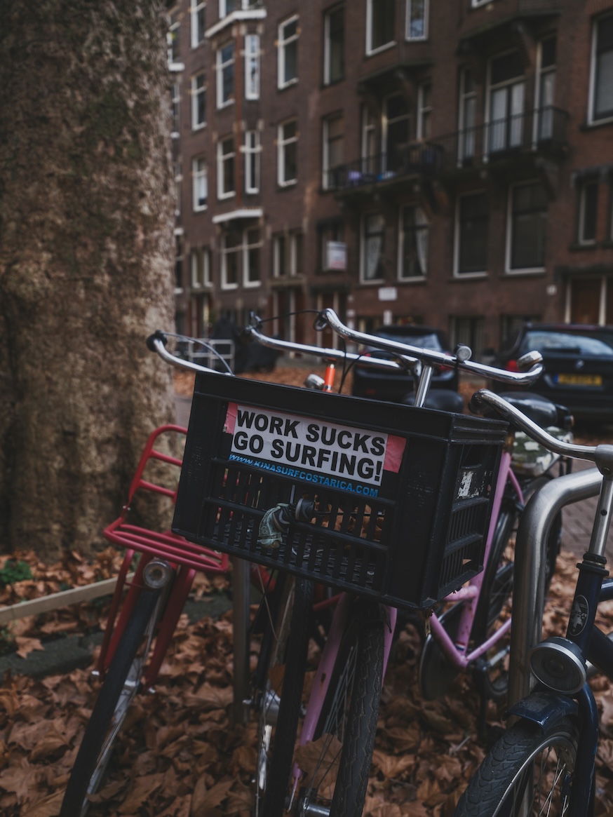 Bikes parked beside a sign saying work sucks go surfing