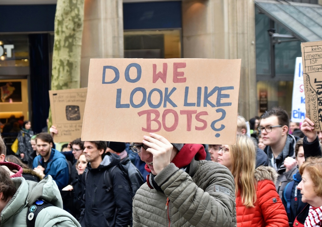 Person holding a cardboard sign asking do we look like bots